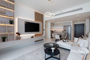 Een moderne woonkamer met een flatscreen televisie, een bank, een salontafel en een keuken op de achtergrond.