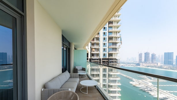 Een balkon met een bank, twee tafeltjes en uitzicht op een jachthaven en de stadslijn.
