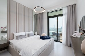 A modern hotel room with a large bed, a view of the city, and a balcony with a table and chairs.