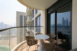 A balcony with wicker furniture and a glass railing overlooking a cityscape.