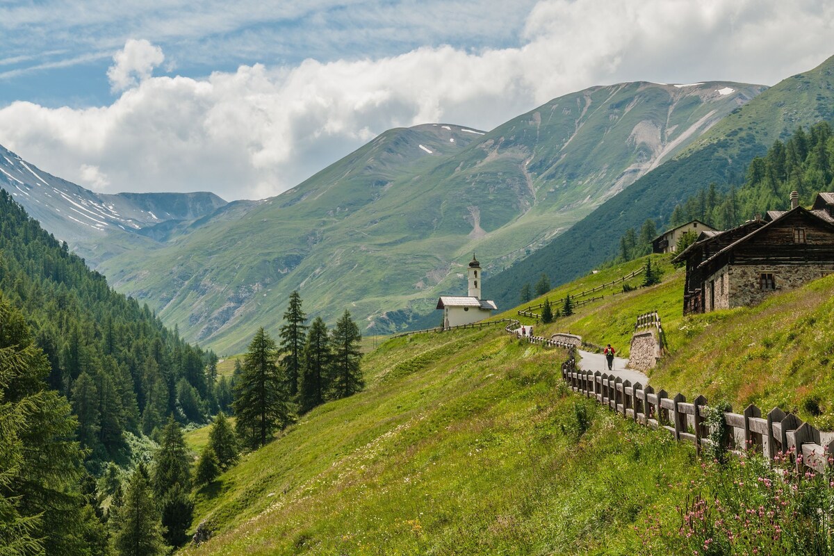 Un paysage de montagne avec un chalet en bois et une petite église sur le flanc d’une colline.