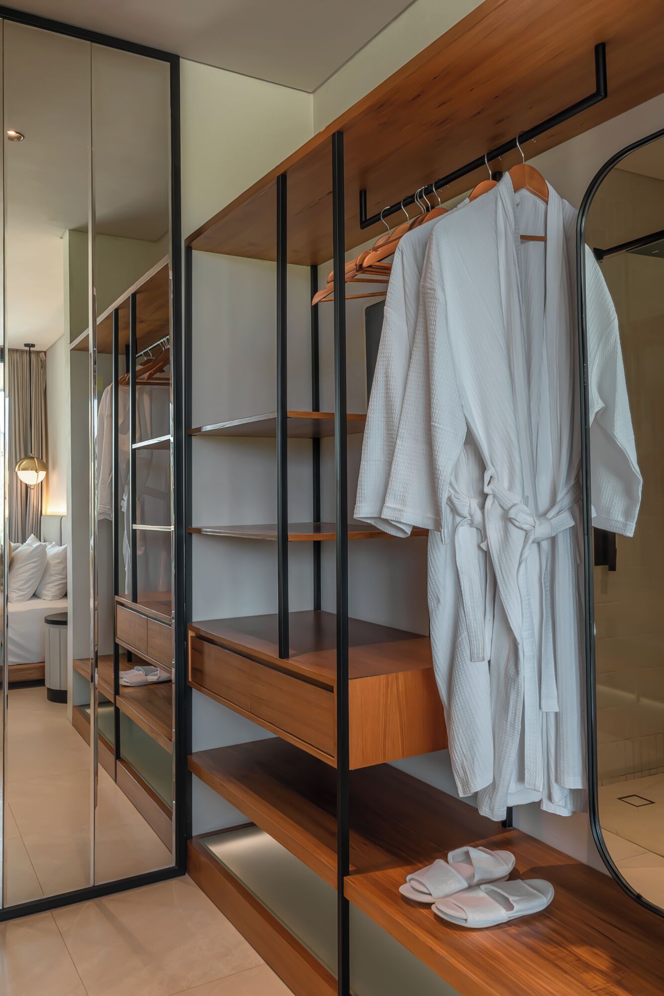 A modern hotel room with a walk-in closet, wooden shelves, and a mirror.