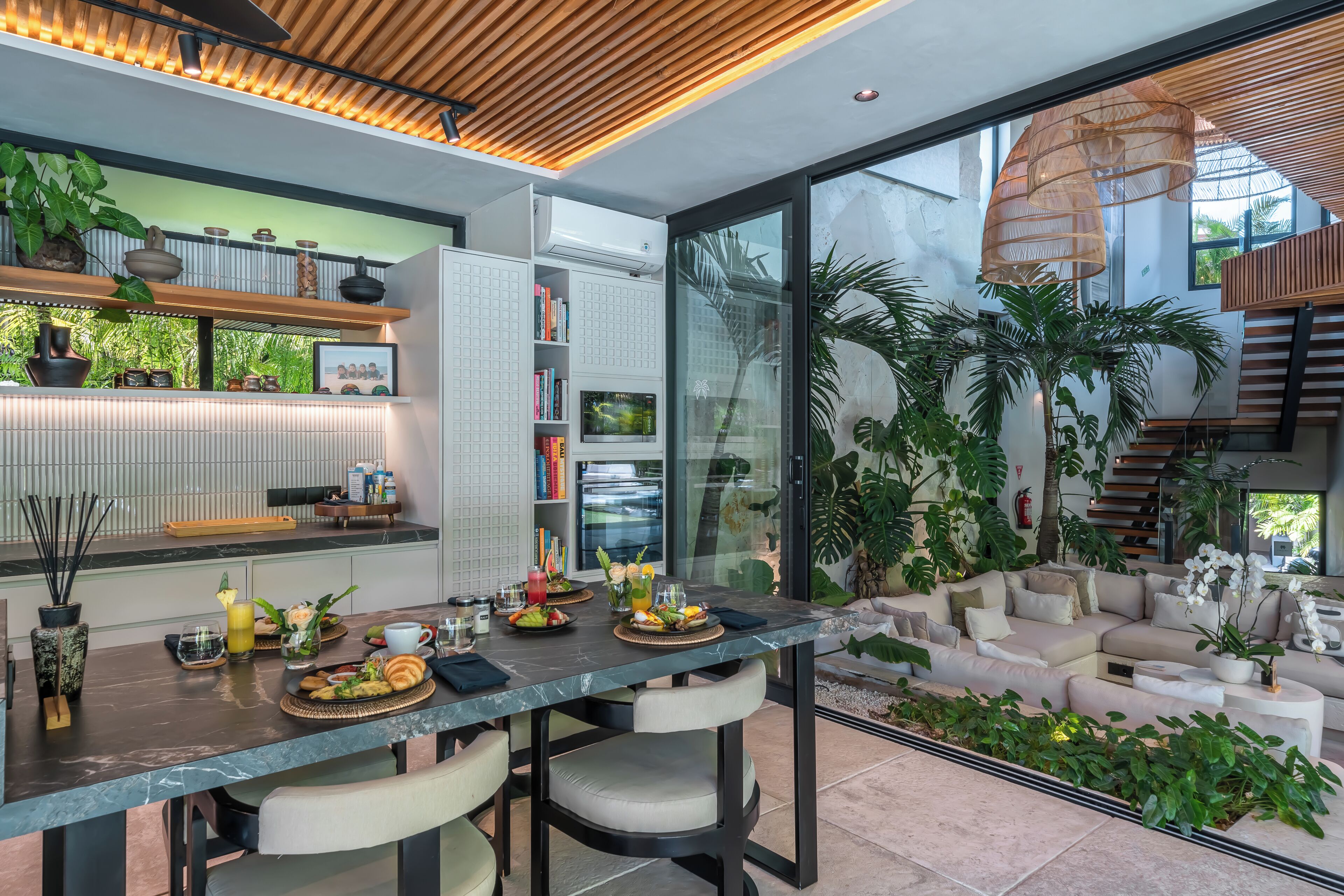 Cozinha moderna com bancada de mármore, área de refeições com cadeiras e uma grande janela com vista para um jardim exuberante.