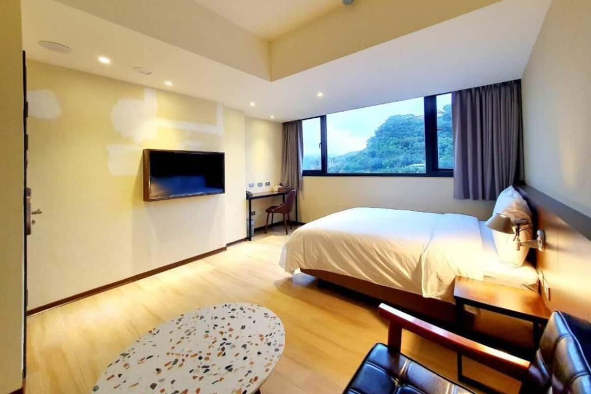Una habitación de hotel moderna con una cama, escritorio, silla y televisor.