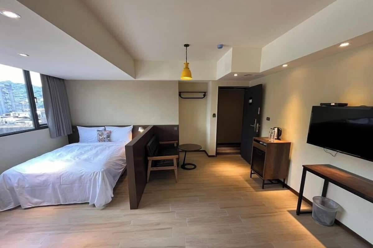 Una habitación de hotel moderna con una cama, un escritorio, una silla, un televisor y vistas a la ciudad.