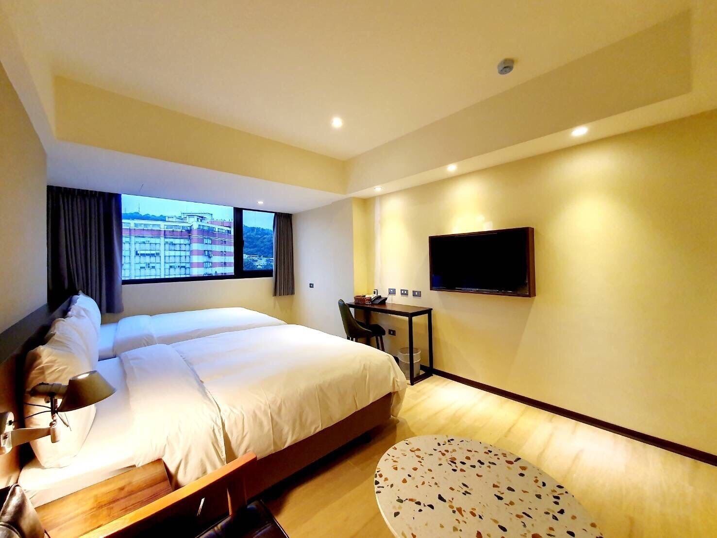 A hotel room with a bed, a desk, a chair, a TV, and a window with a city view.