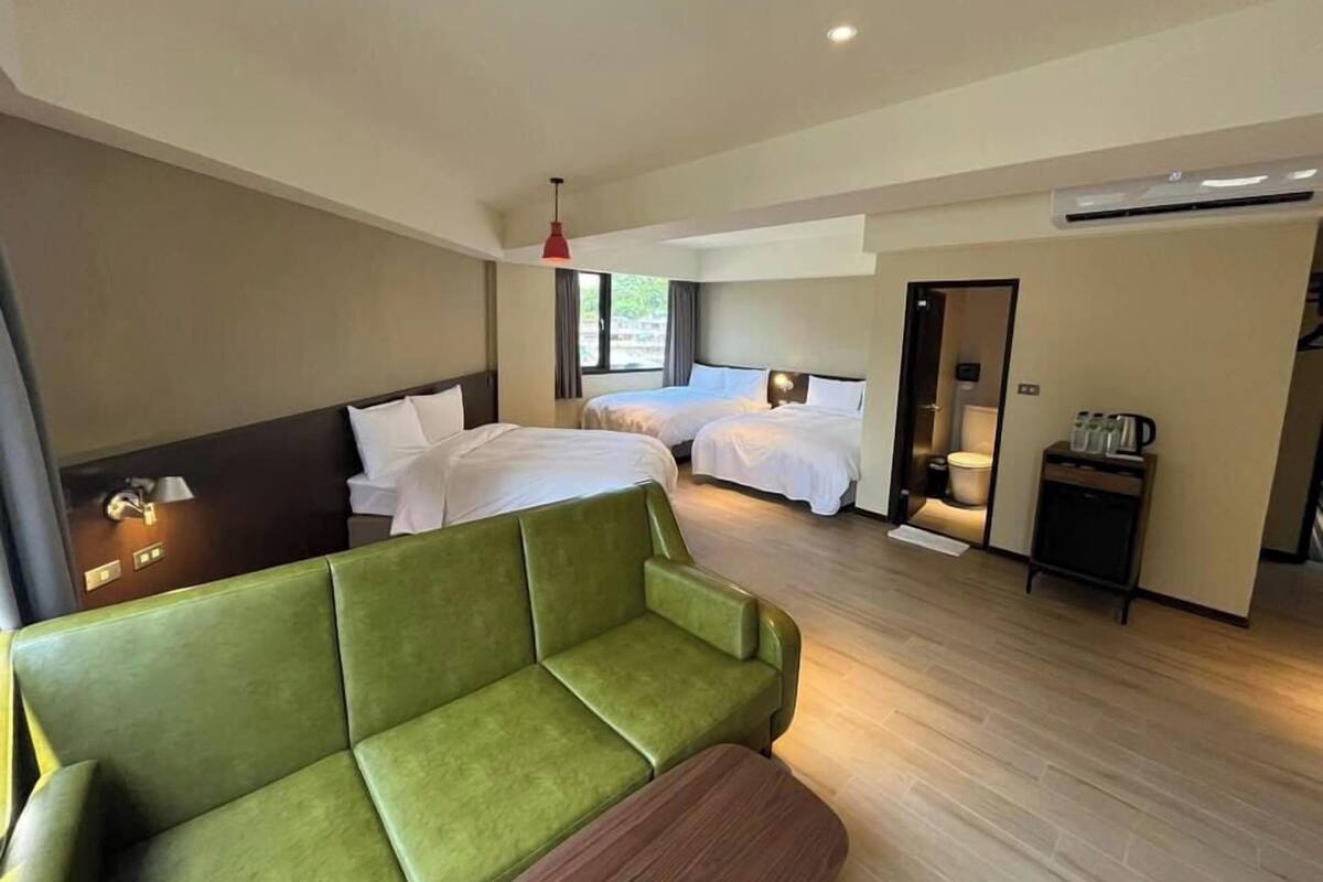 Habitación de hotel con dos camas, un sofá verde, una mesita y una estación de café.