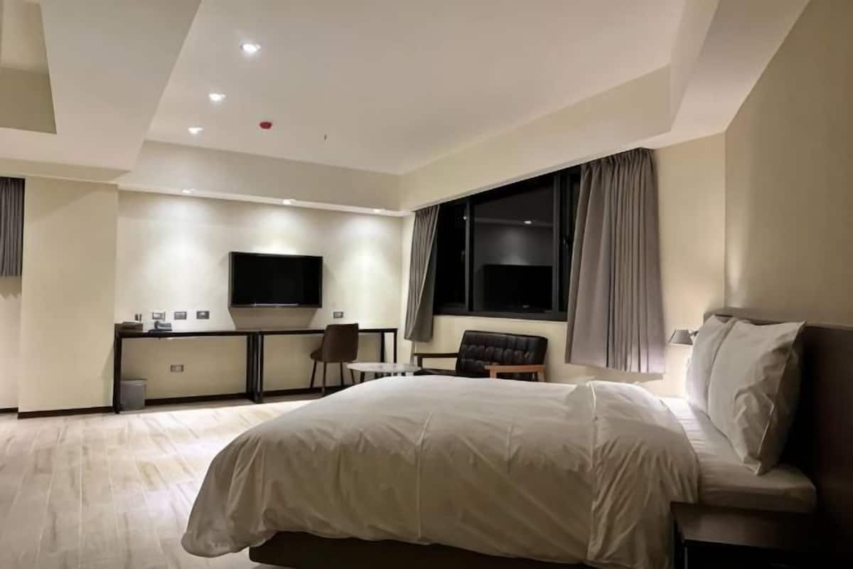 Una habitación de hotel con una cama grande, un escritorio con silla, un televisor y una ventana con cortinas.