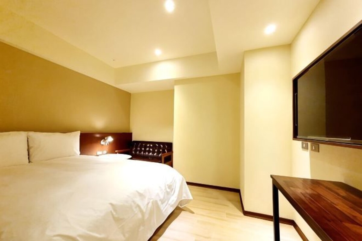 Una habitación de hotel con una cama grande, un televisor en la pared y una mesita de noche de madera.