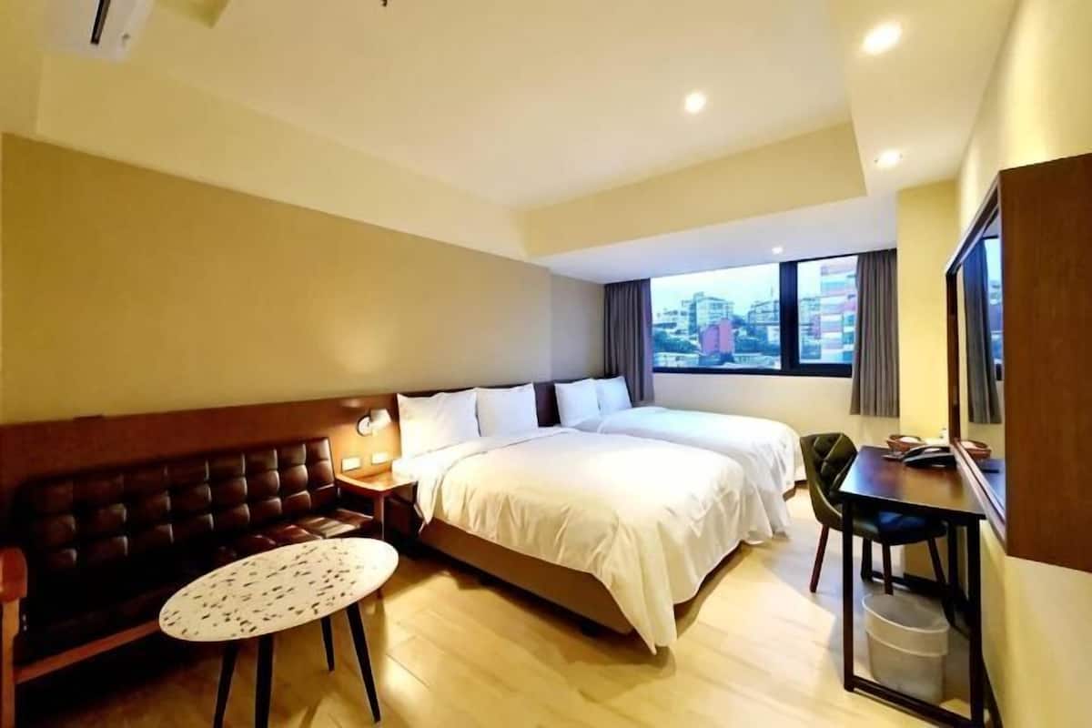 Habitación de hotel con cama, escritorio, silla, mesita y ventana con vista a la ciudad.