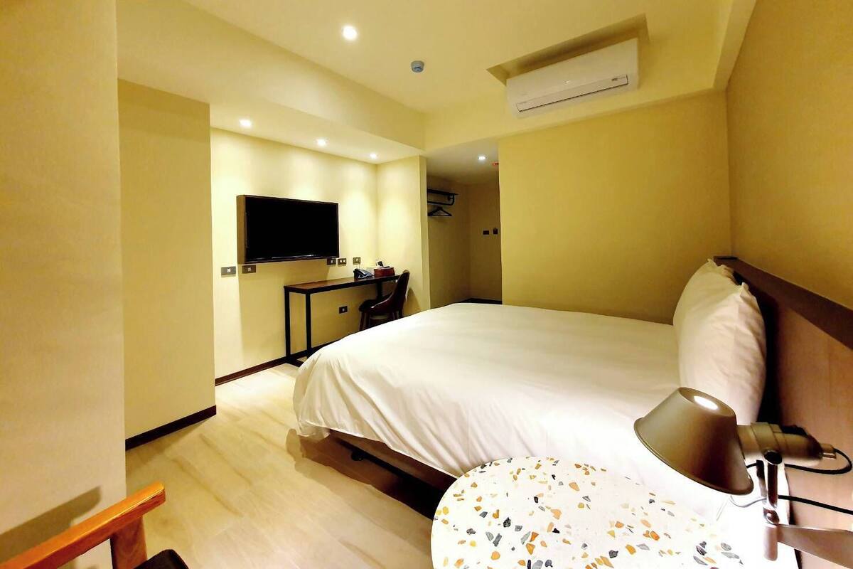Habitación de hotel con una cama grande, un escritorio con silla, un televisor montado en la pared y un equipo de aire acondicionado.