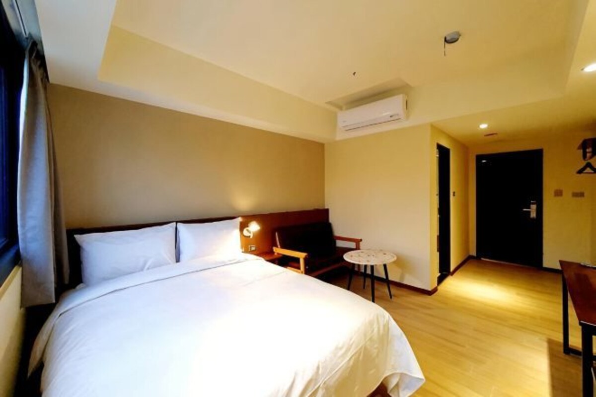 Una habitación de hotel con una cama, una mesita, una silla y un aire acondicionado.