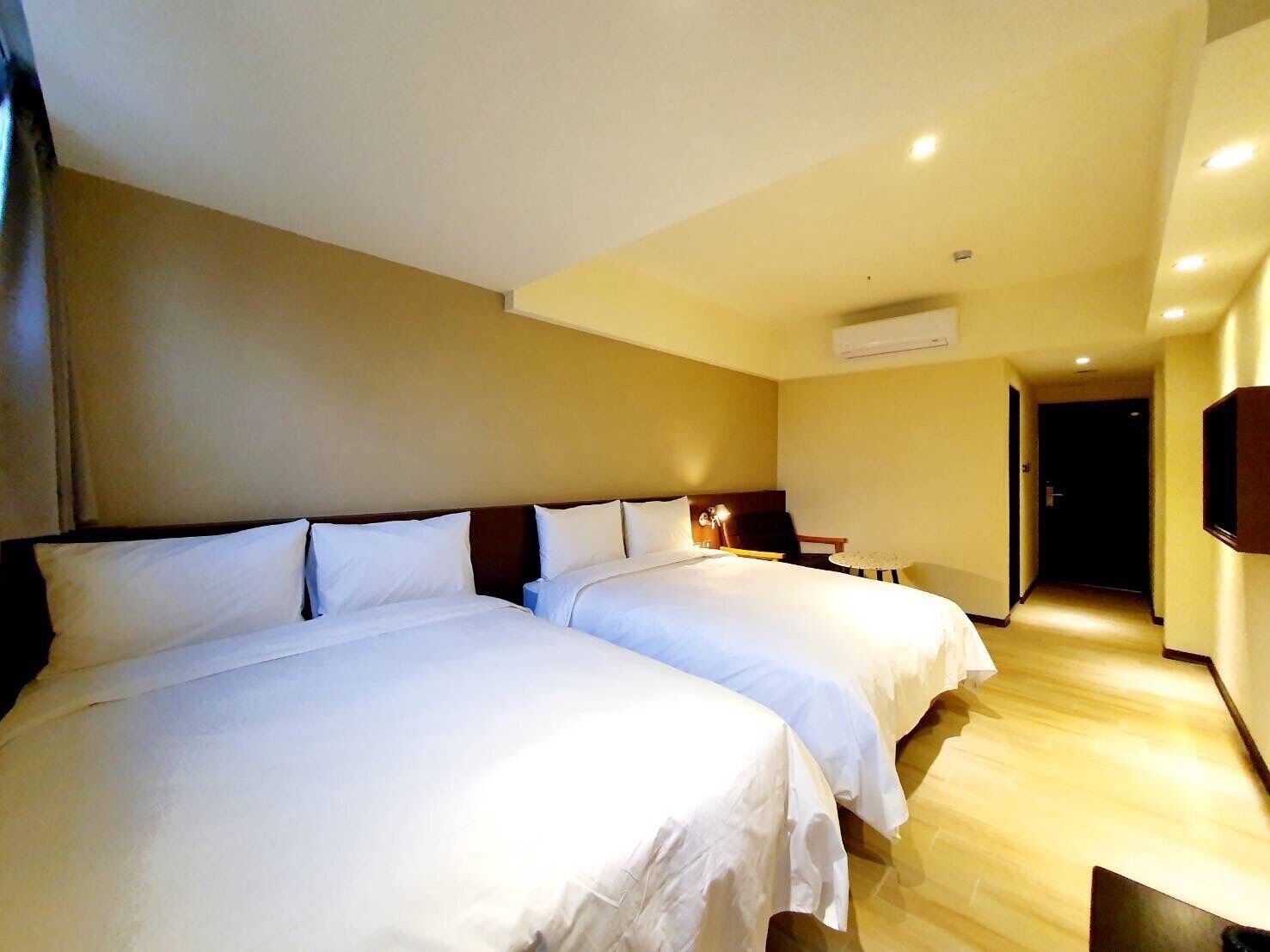 Quarto de hotel com duas camas, piso de madeira e aparelho de ar condicionado na parede.