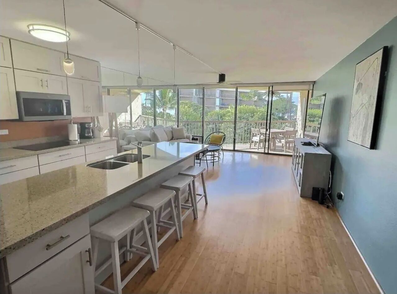 A modern kitchen with a large island, bar stools, and a view of the outdoors.