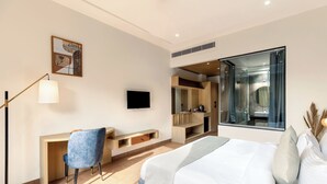 A modern hotel room with a large bed, a desk, a chair, a TV, and a bathroom visible through a glass door. - The Montail Udaipur (Udaipur)