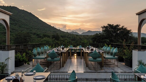 An outdoor dining area with tables and chairs, surrounded by greenery and hills. - The Montail Udaipur (Udaipur)