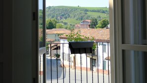 A view from a balcony with a metal railing, overlooking a street with buildings and a green landscape in the distance. - Albergo Tenco by Bottega (Ricaldone)