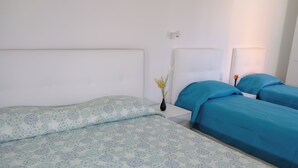 A bedroom with two beds, one with a patterned bedspread and the other with a solid blue bedspread. There is a nightstand with a vase of flowers between the beds. - Albergo Tenco by Bottega (Ricaldone)