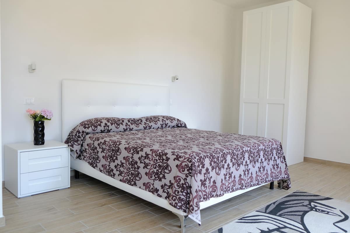 Un dormitorio con cama, mesita de noche, un jarrón con flores y un armario.