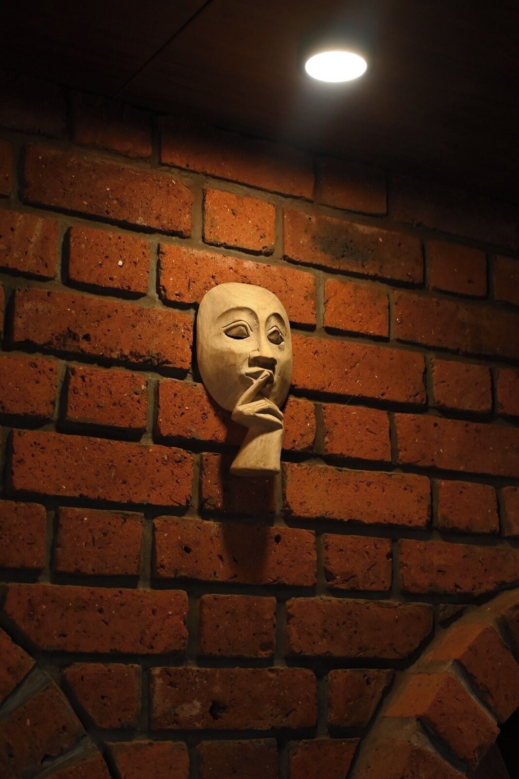 Una pared de ladrillo con una escultura de madera fijada en ella.
