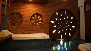 A room with a brick wall, two circular wooden doors with cut-out patterns, a bed, and a small table with towels. - Bamboo and Bricks Resorts (Paud)