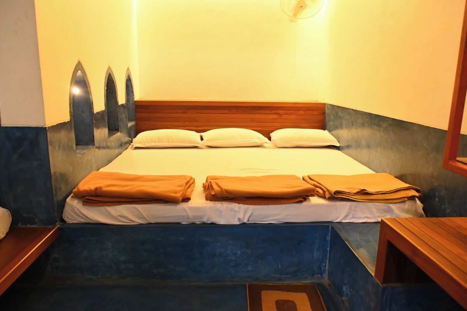 Una cama bien tendida con sábanas blancas y toallas marrones, cabecera de madera y una pared con un diseño decorativo.
