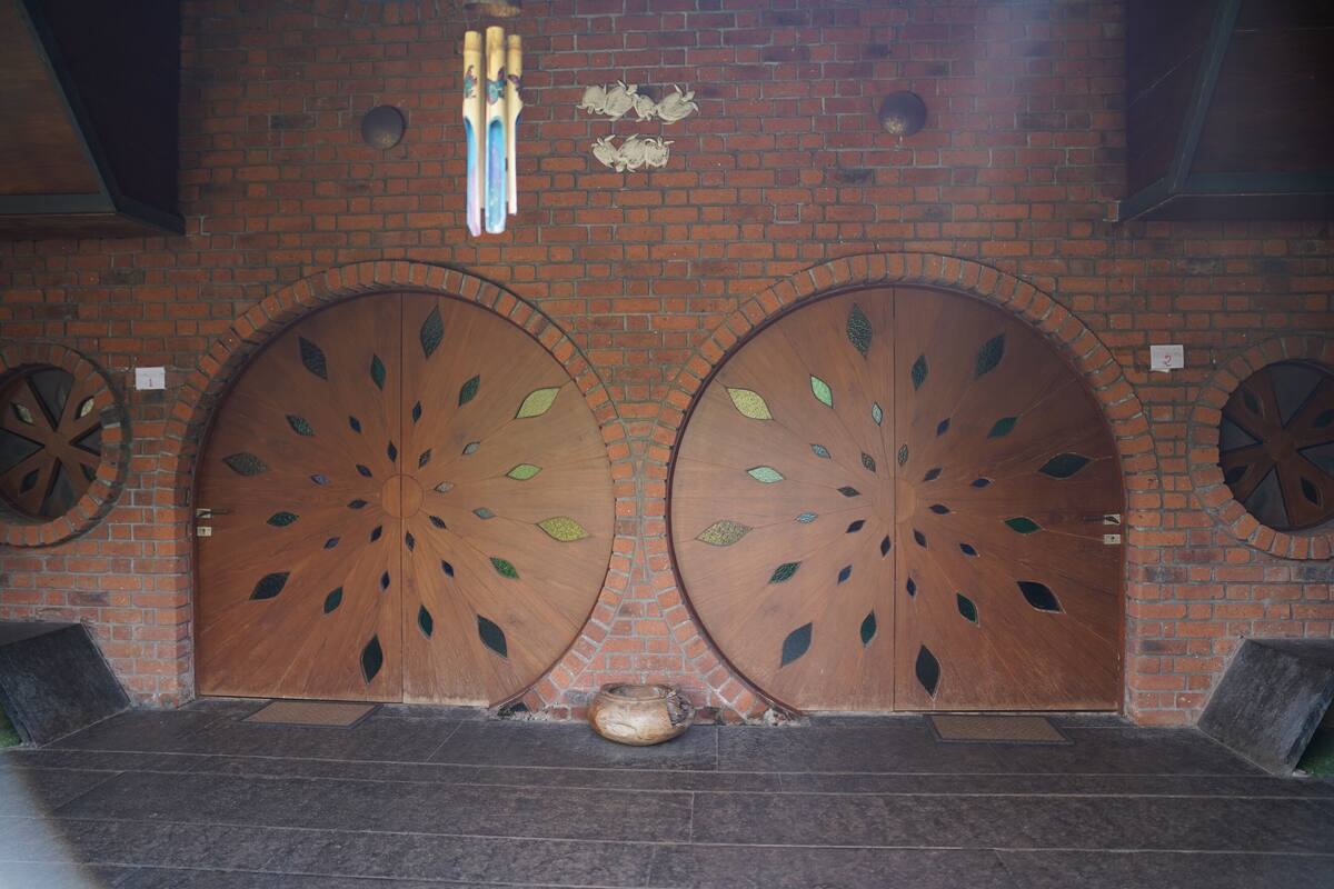 A large wooden door with a circular design and a small pot on the ground in front.