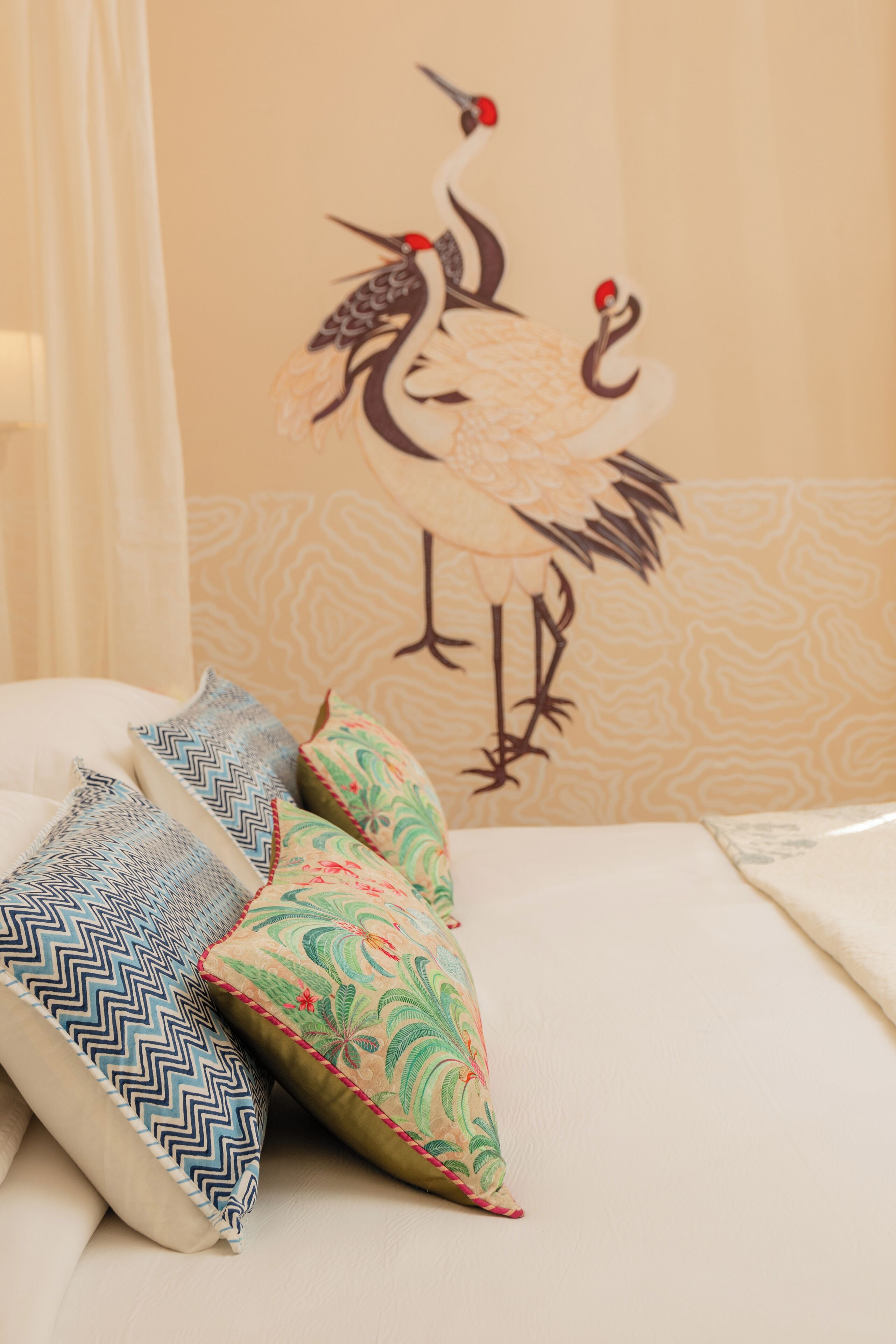 Una cama con almohadones decorativos y un mural de un pájaro en la pared.