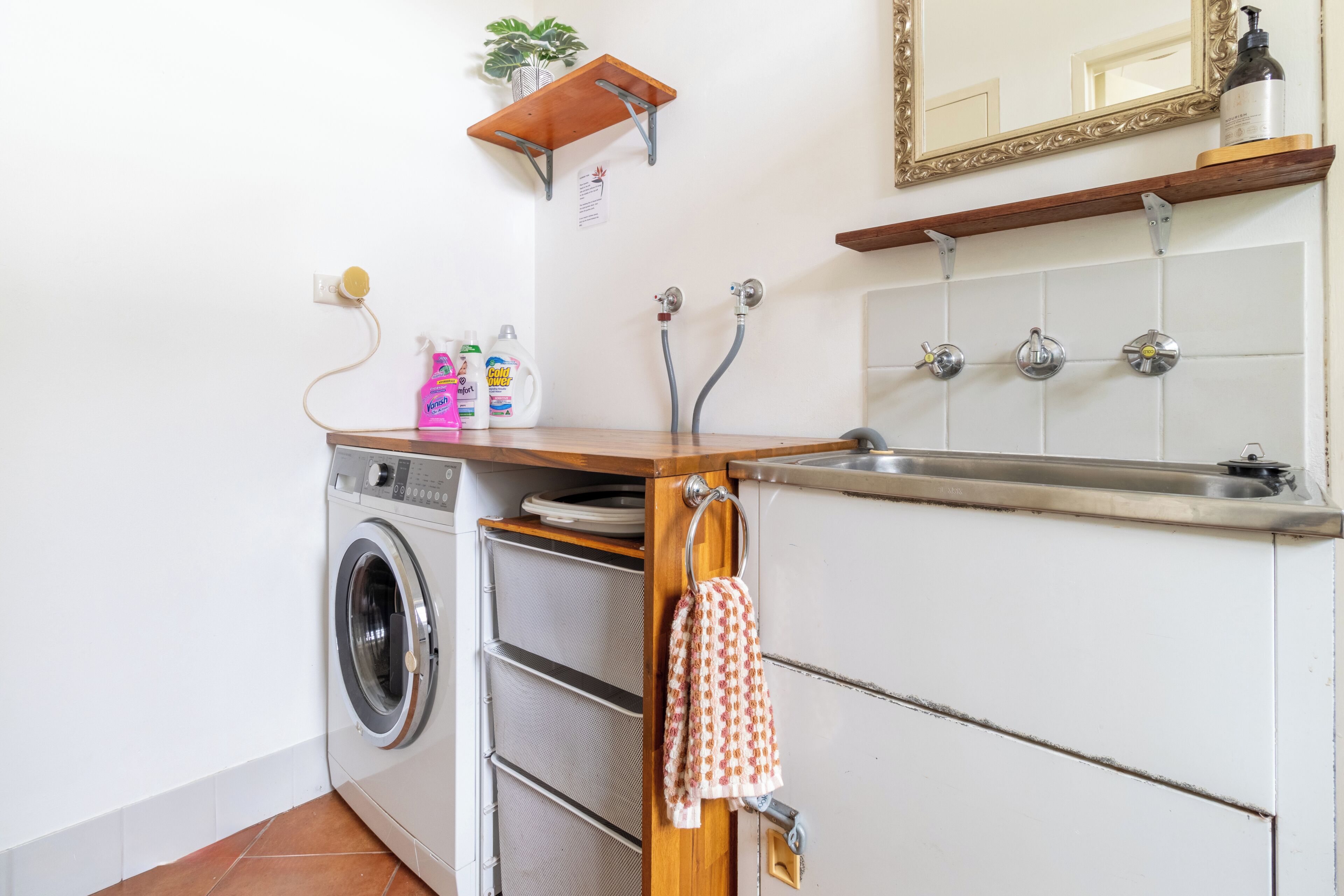 A compact laundry area with a washing machine, drying racks, a sink, and a mirror.