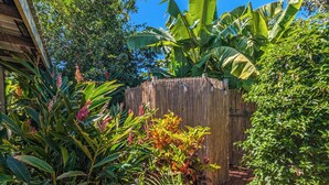 A garden with a variety of plants, a bamboo fence, and a wooden structure. - Tropical Treasure | Outdoor Kitchen & Shower (Wanguri)