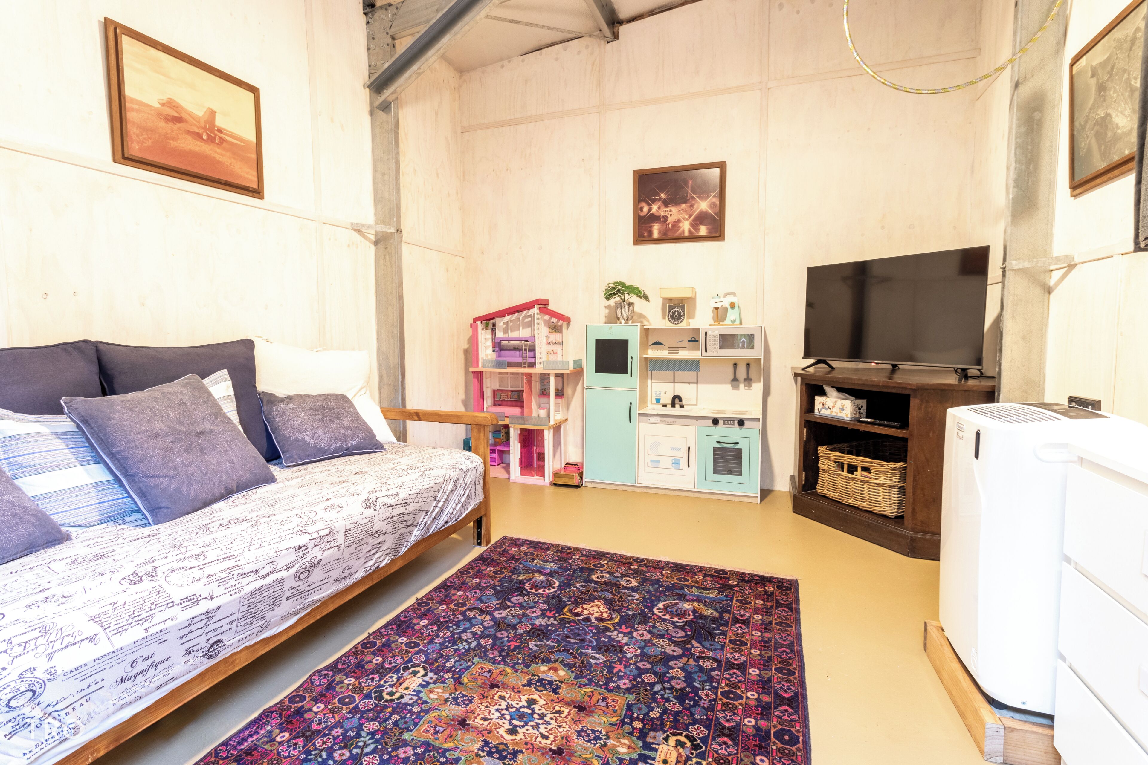 A bedroom with a bed, a TV, a refrigerator, and a kitchen area.