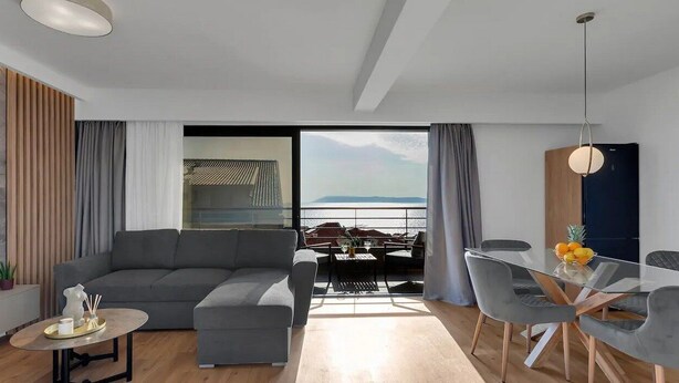Un salon moderne avec un canapé gris, une petite table ronde et un coin repas comprenant une table en verre et des chaises grises.