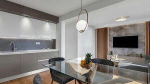 Une cuisine moderne avec des meubles gris, un évier en acier inoxydable et une table à manger en verre, accompagnée de chaises.