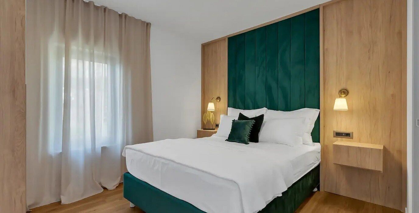 Un letto rifatto con lenzuola bianche e biancheria da letto color petrolio, illuminato da due abat-jour.