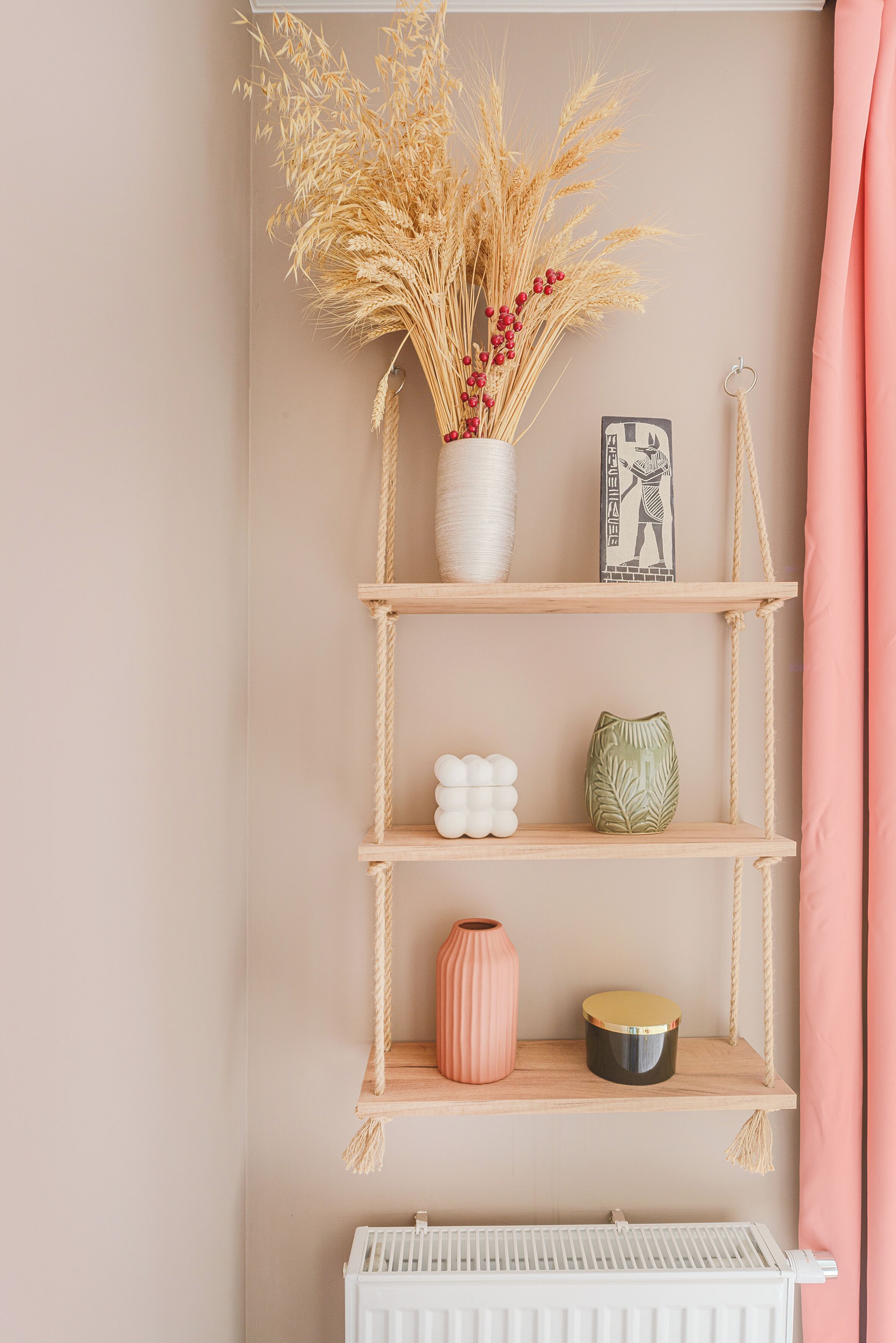 A wall-mounted wooden shelf with decorative items, including a vase with dried plants and a framed picture.