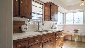 A kitchen with wooden cabinets, a double sink, and a glass table. - 4-bed designer family-friendly home with large yards & theater room near beaches (Los Angeles)