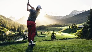 A person playing golf on a sunny day with a mountainous background.