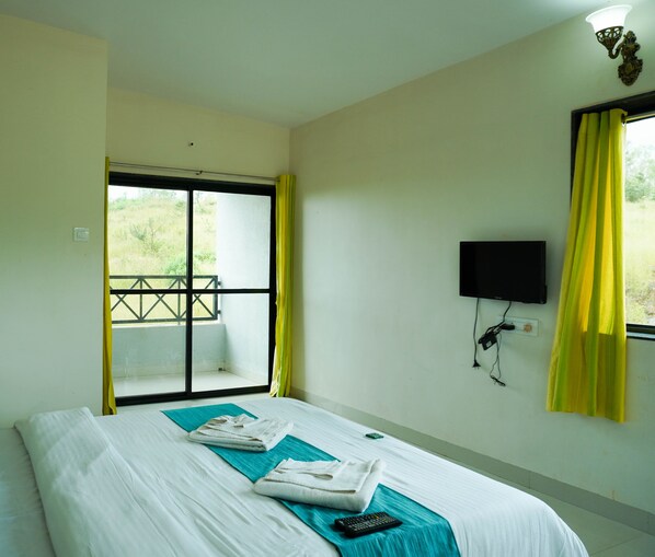 A hotel room with a bed, a TV mounted on the wall, and a window with yellow curtains. - Forest Leaf (Mahabaleshwar)