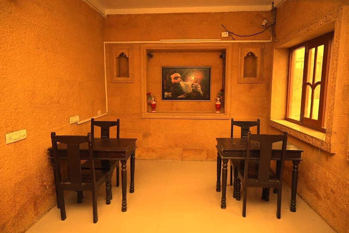 A dining area with a table and chairs, a framed picture on the wall, and a window with decorative elements.