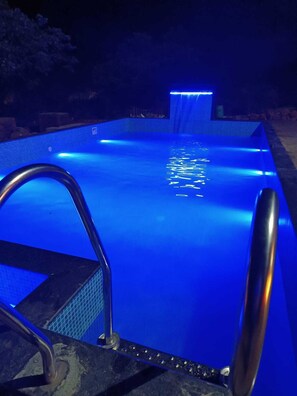 Una piscina con una fuente iluminada en azul y una escalera metálica que da al agua.