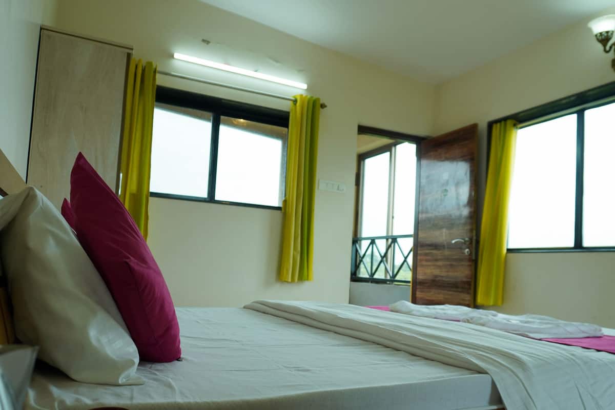 A hotel room with two beds, a wooden wardrobe, a window with yellow curtains, and a door with a metal grille.