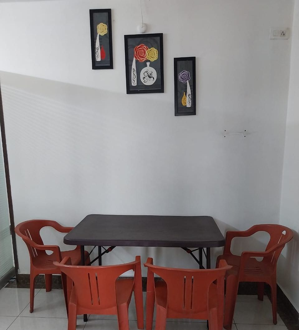 Un comedor con una mesa y cuatro sillas, tres obras de arte enmarcadas en la pared y un enchufe.