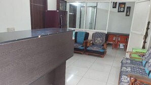 Ein Empfangsbereich mit einem Holzbüro, zwei gemusterten Sesseln, einem Sofa und einem Schrank.
