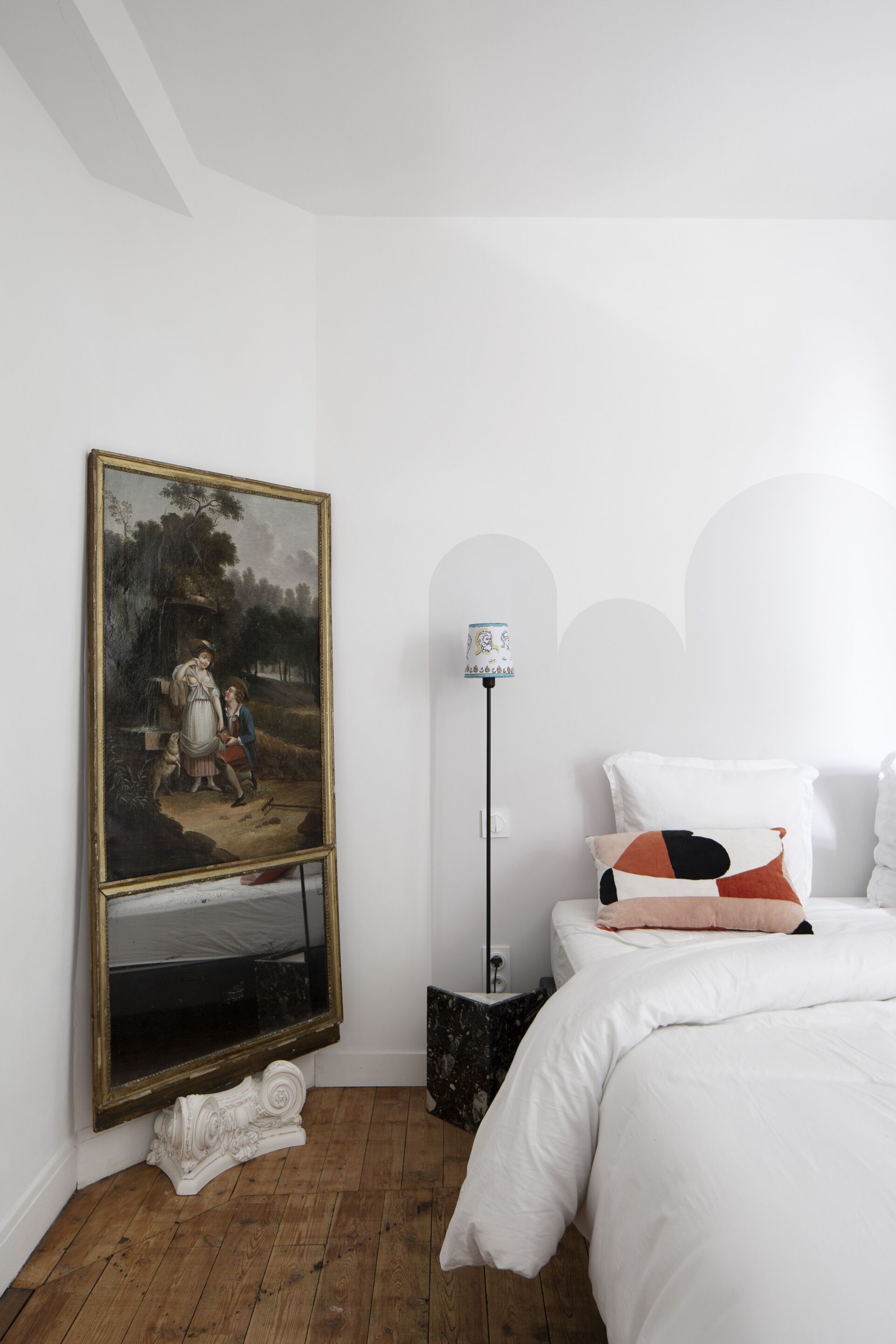 A bedroom with a large classical painting, a modern lamp, and a neatly made bed.