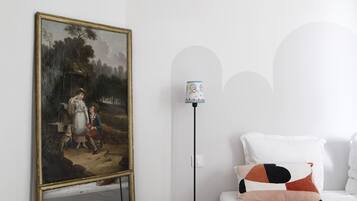 A bedroom with a large classical painting, a modern lamp, and a neatly made bed.