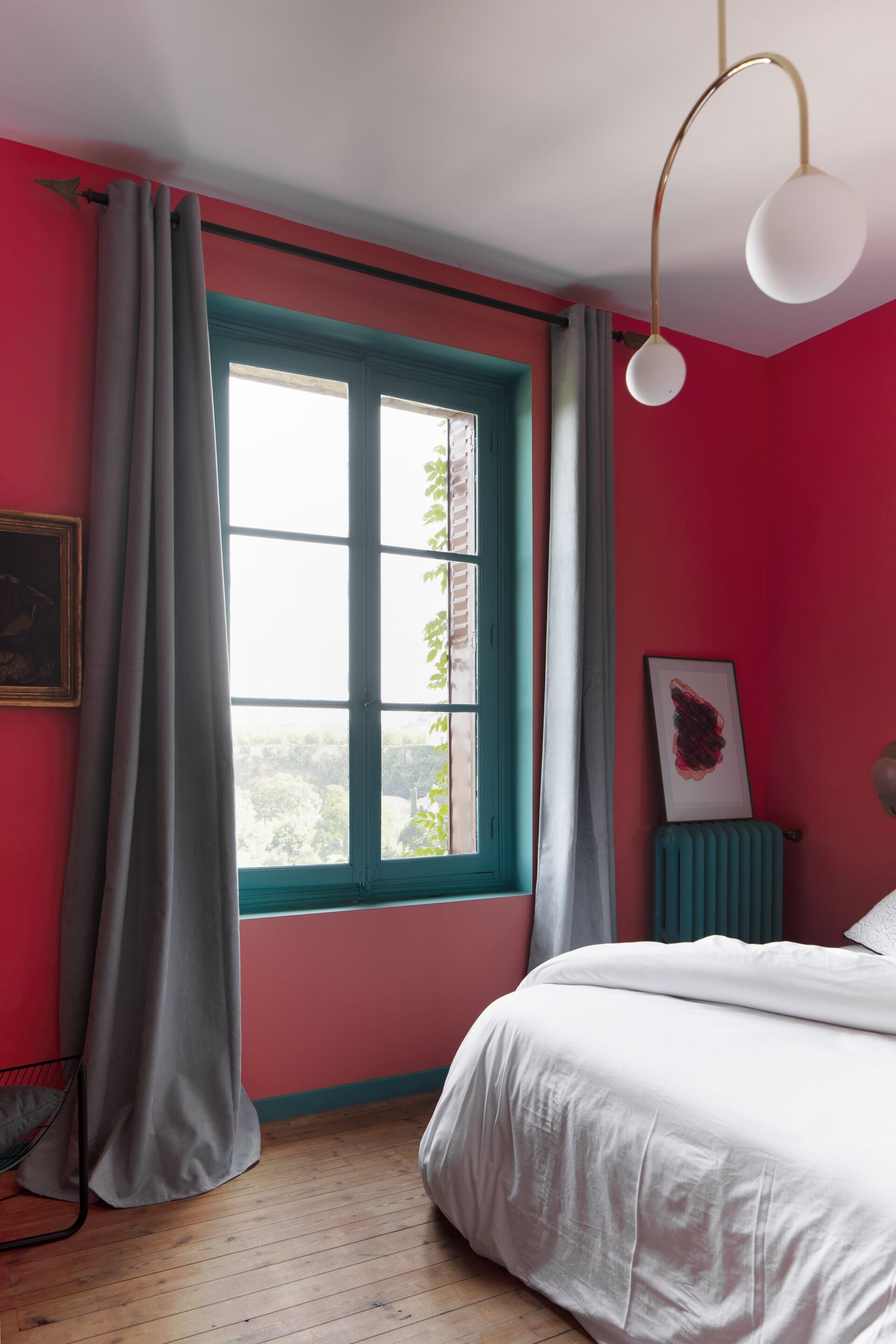 Une chambre à coucher avec un lit, une fenêtre avec des rideaux, un radiateur et un luminaire fixé au mur.