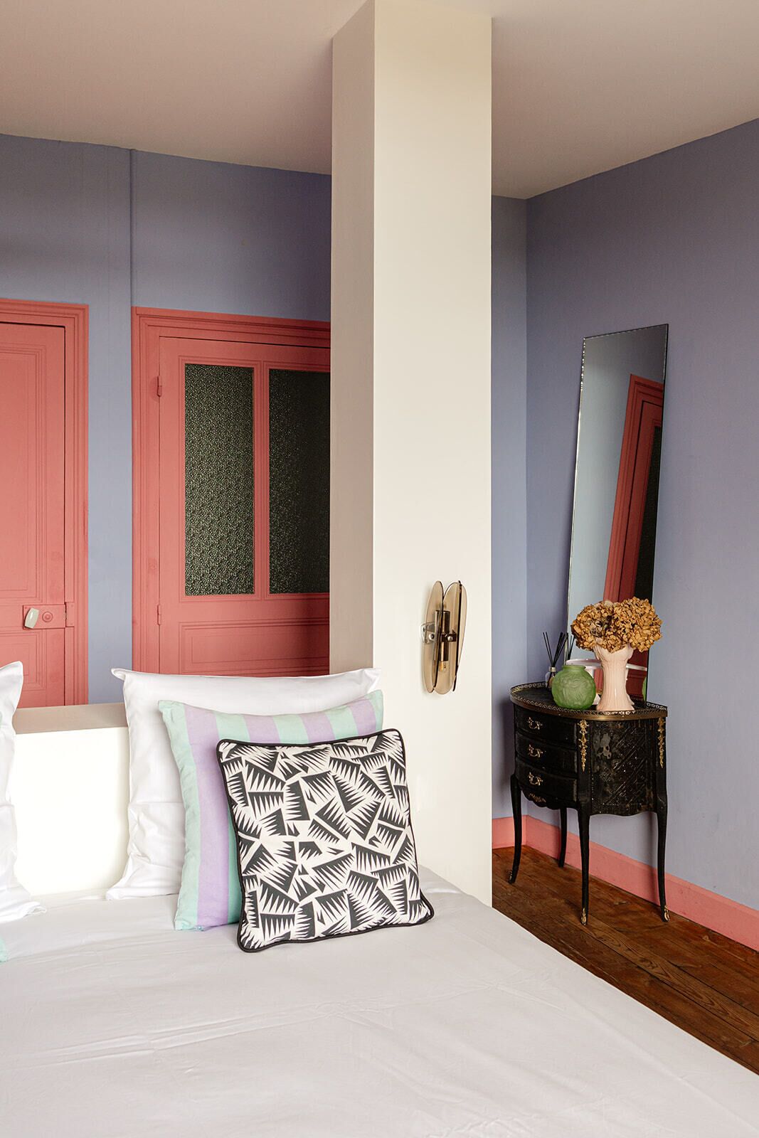 Un dormitorio con cama, almohadas, cómoda, espejo y puerta.