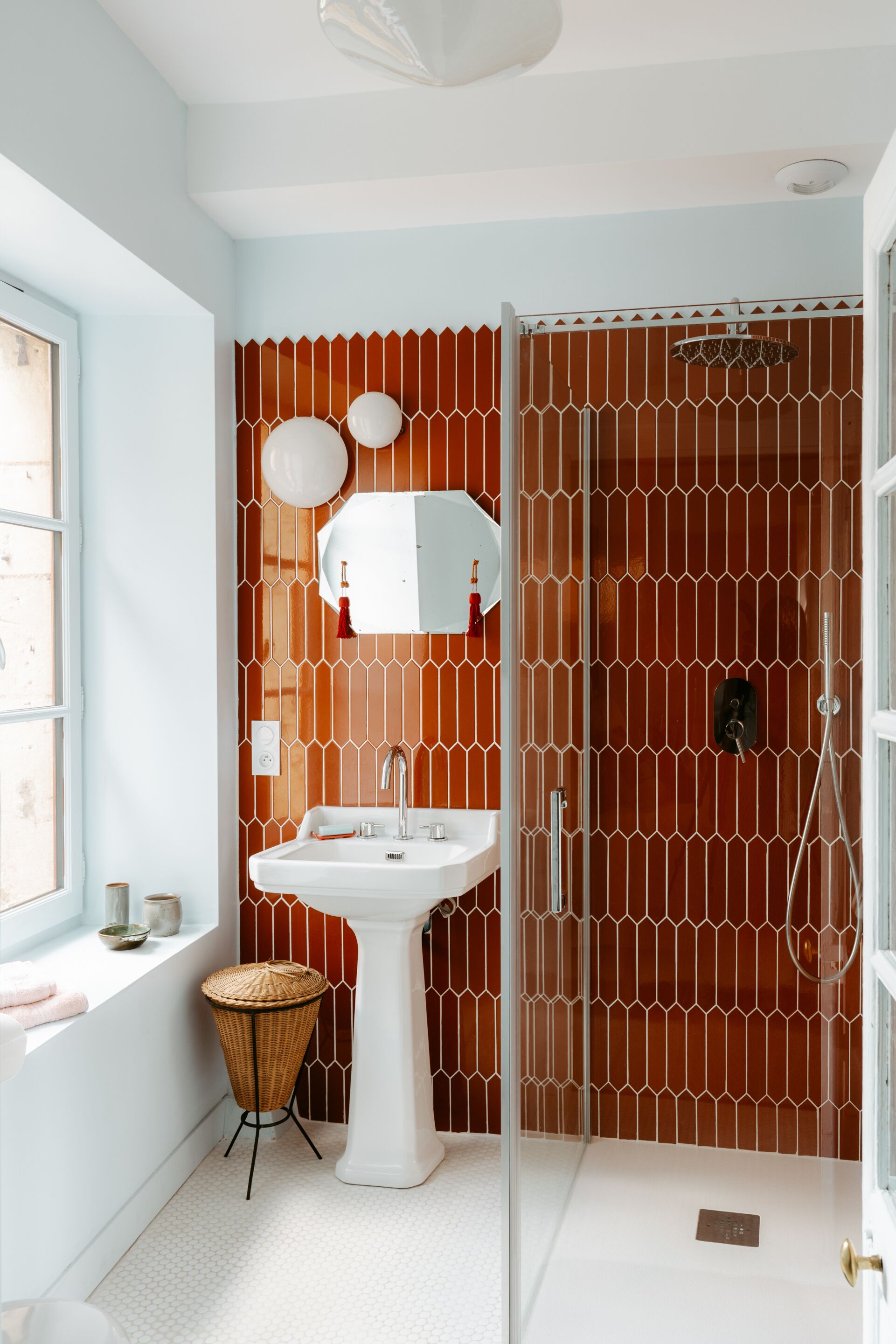 Un baño con lavamanos blanco, espejo y cabina de ducha con revestimiento estampado.