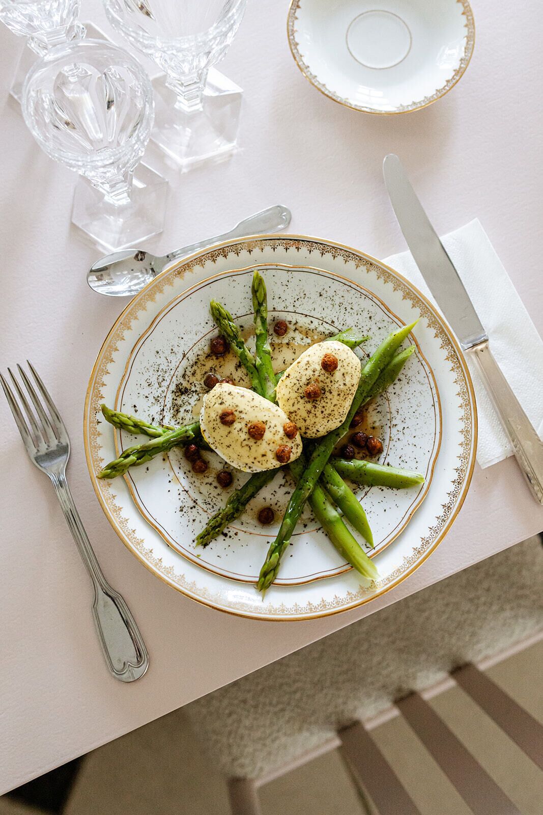 A plate of food with asparagus and a white plate with a gold rim.