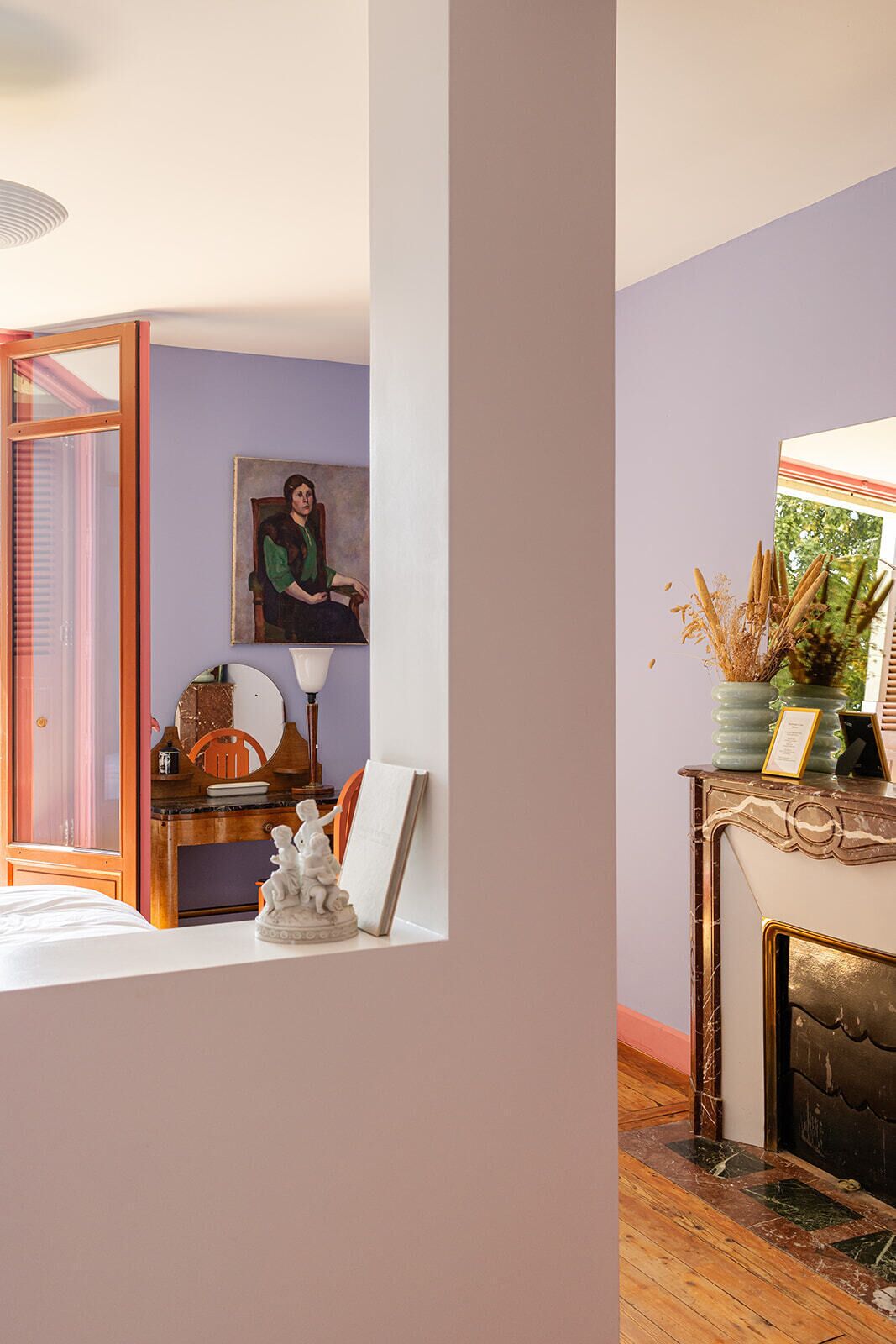 A room with a wooden floor, a desk with a lamp, a chair, and a painting on the wall.